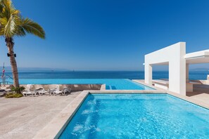 A swimming pool with a view of the ocean, lounge chairs, and a palm tree. - Entire condo in Puerto Vallarta, Mexico (Puerto Vallarta)
