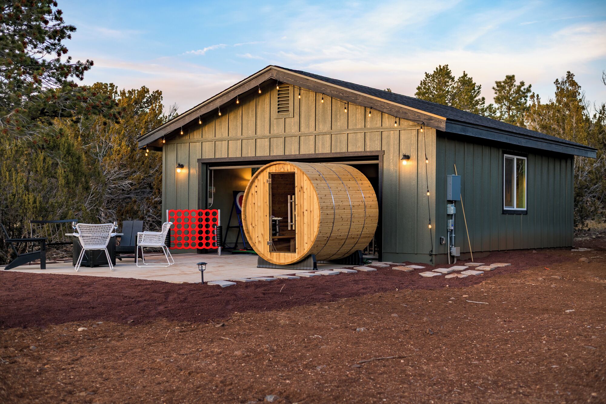 Un bâtiment rustique avec une grande entrée en forme de tonneau en bois, des places assises à l’extérieur et une clôture rouge.