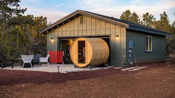 Un bâtiment rustique avec une grande entrée en forme de tonneau en bois, des places assises à l’extérieur et une clôture rouge.