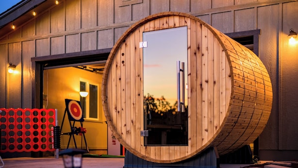 A wooden barrel-shaped structure in front of a building with a garage door. - Gateway Getaway in wonderful Williams with fire pit, sauna, game room and views! (Williams)