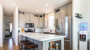 A modern kitchen with stainless steel appliances, wooden stools, and a water dispenser. - Gateway Getaway in wonderful Williams with fire pit, sauna, game room and views! (Williams)