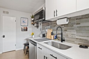 A modern kitchen with white cabinets, a stainless steel sink, a microwave, and a tiled backsplash.