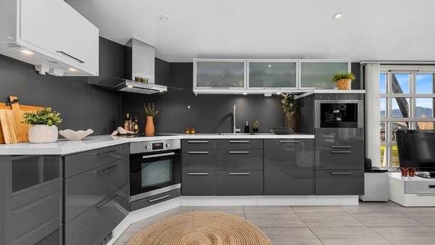 Une cuisine moderne avec des meubles de couleur gris foncé, un plan de travail blanc et un four encastré.