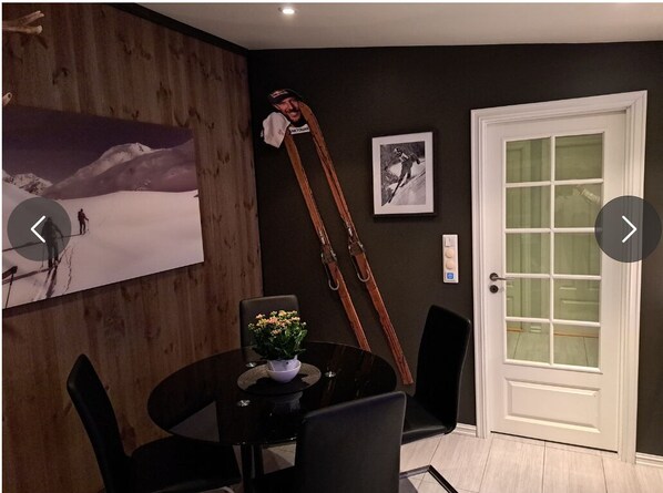 A dining area with a round table, black chairs, a potted plant, ski equipment, and a door with frosted glass panels. - Cozy apartment Ski in-out, Downhill in-out, within walking distance to the center of Oppdal (Trøndelag)