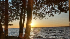 A beach scene with trees and the sun setting over the water. - Charming 2-bedroom house in Shawano with AC, WiFi (Shawano)