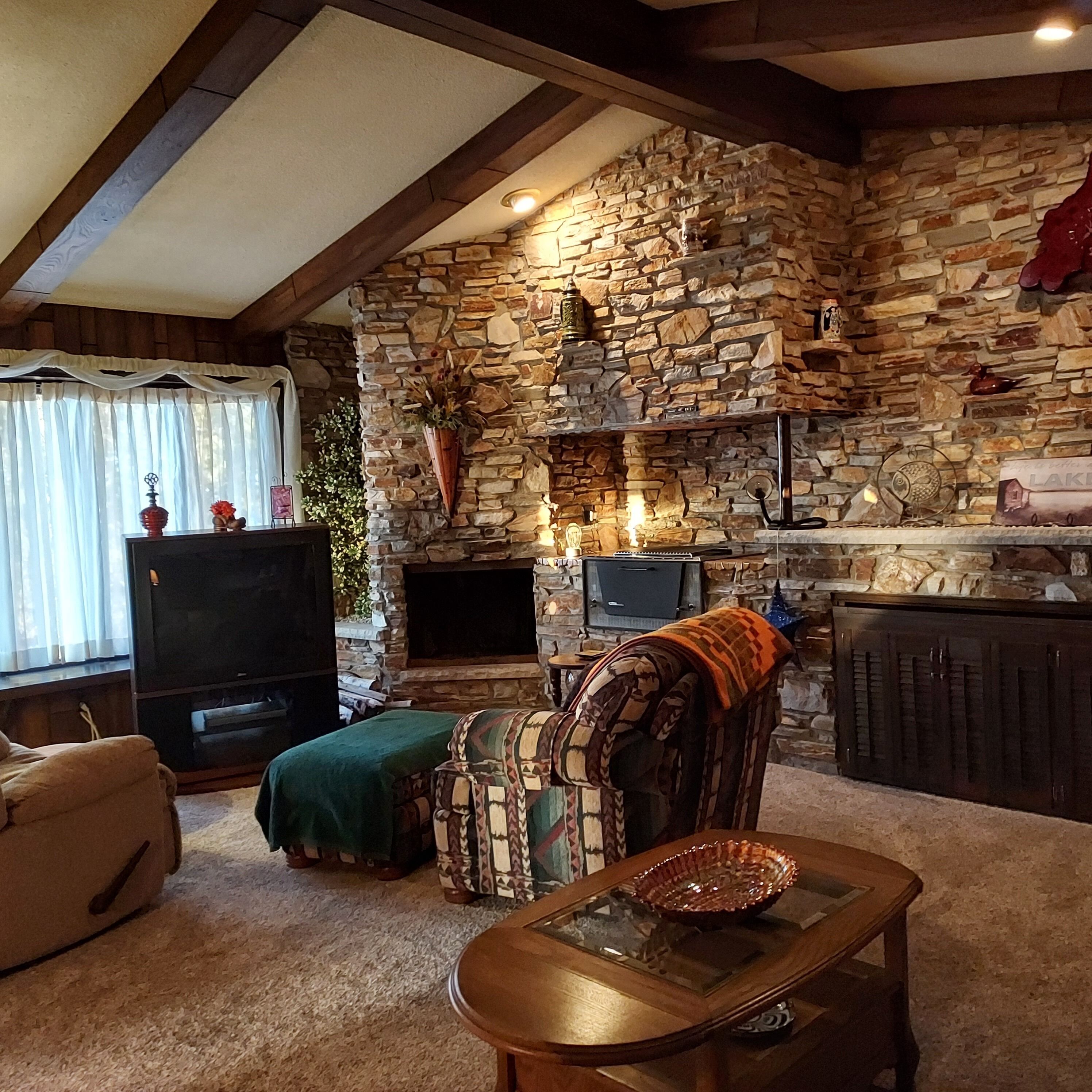 A cozy living room with a stone fireplace, a television, and a dining table with a glass top.