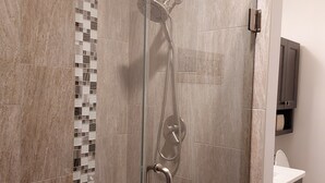A modern bathroom with a glass-enclosed shower, a tiled wall with a mosaic pattern, and a white sink with a cabinet. - Charming 2-bedroom house in Shawano with AC, WiFi (Shawano)