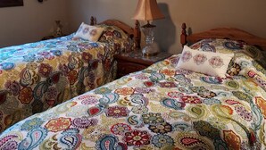 A room with two beds, each with a patterned bedspread, a bedside lamp, and a wall decoration. - Charming 2-bedroom house in Shawano with AC, WiFi (Shawano)