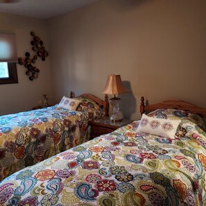 A room with two beds, each with a patterned bedspread, a bedside lamp, and a wall decoration. - Charming 2-bedroom house in Shawano with AC, WiFi (Shawano)