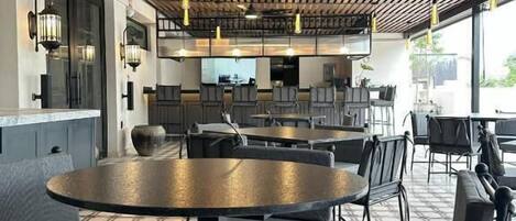 Un comedor moderno con techo de madera, mesas redondas y sillas tapizadas en gris.