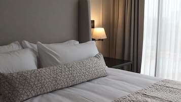Una habitación de hotel con una cama grande, cabecera, mesita de noche con lámpara y ventana con cortinas.