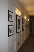 Un pasillo con fotografías blanco y negro enmarcadas en la pared, iluminación empotrada y suelo de madera.