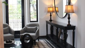 A hotel lobby with two armchairs, a console table with lamps, a large mirror, and a patterned floor.