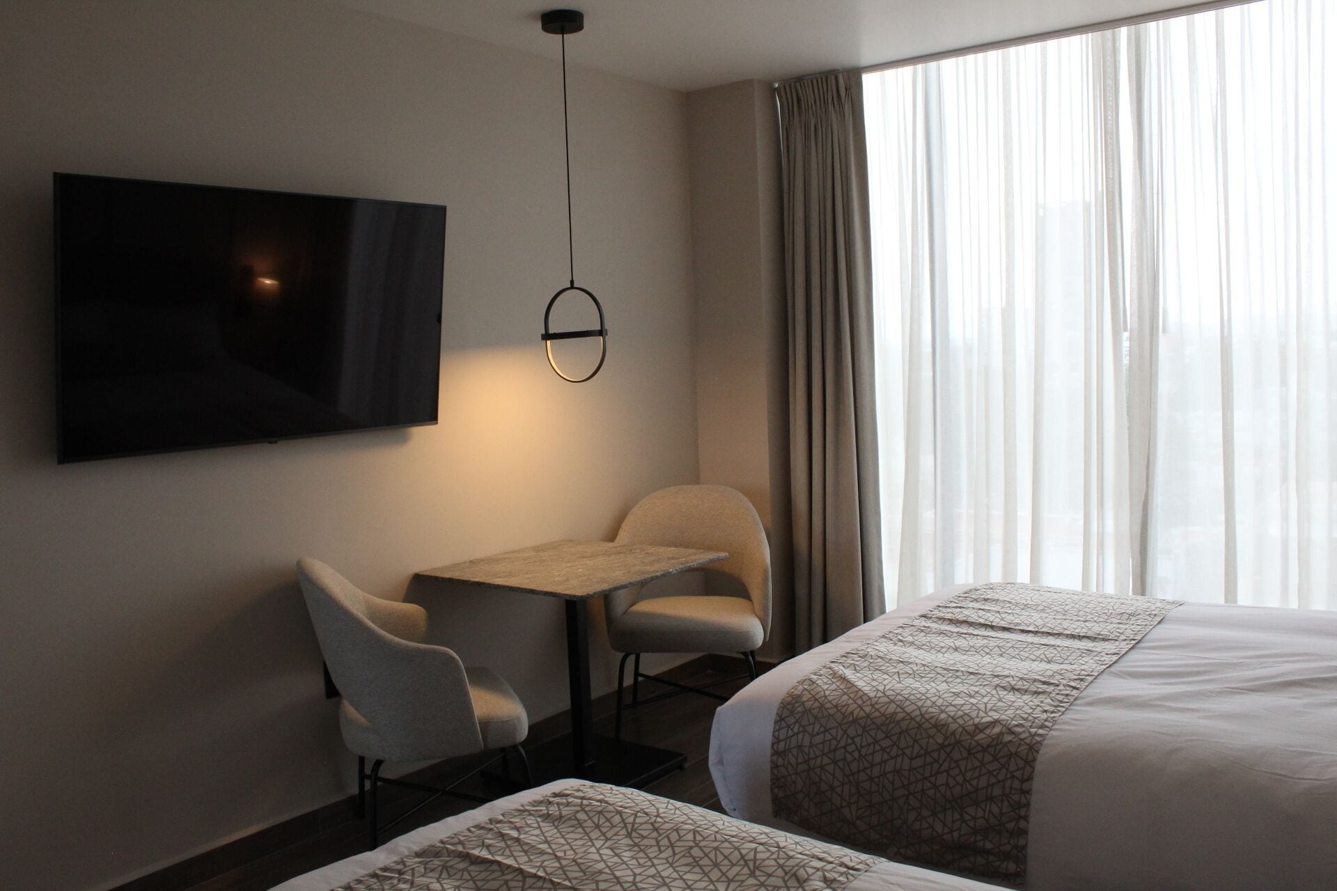 A hotel room with a bed, a desk, two chairs, a TV, and a window with curtains.