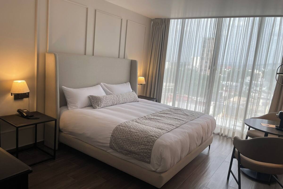 Hotelkamer met een groot bed, twee bedlampen, een telefoon, een klein tafeltje en een stoel.