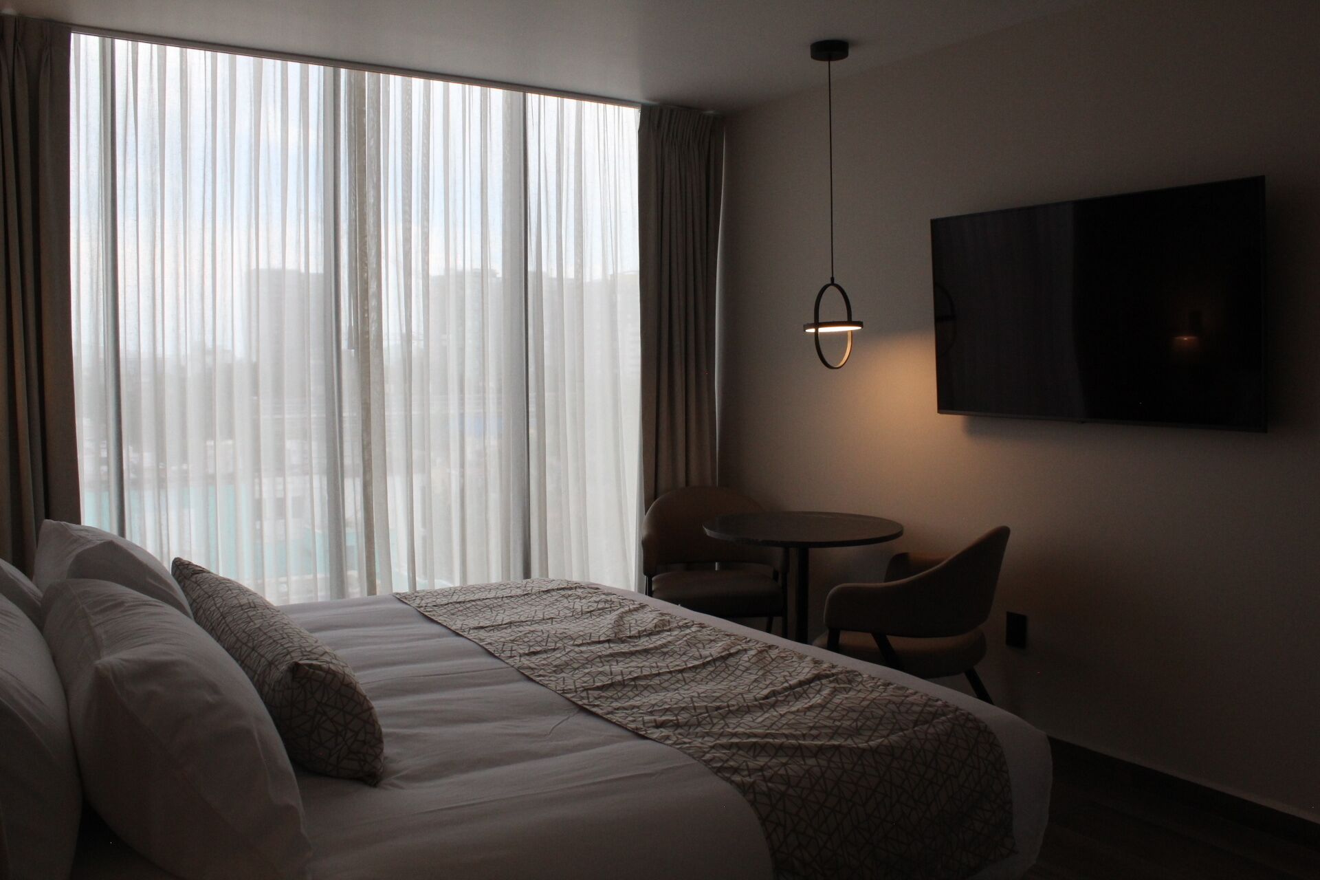 A hotel room with a large bed, a small table, and a TV mounted on the wall.
