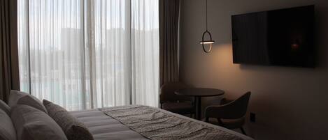 A hotel room with a large bed, a small table, and a TV mounted on the wall.