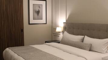 A neatly made bed with a geometric patterned bedspread, a framed abstract artwork on the wall, and a wall-mounted air conditioner.