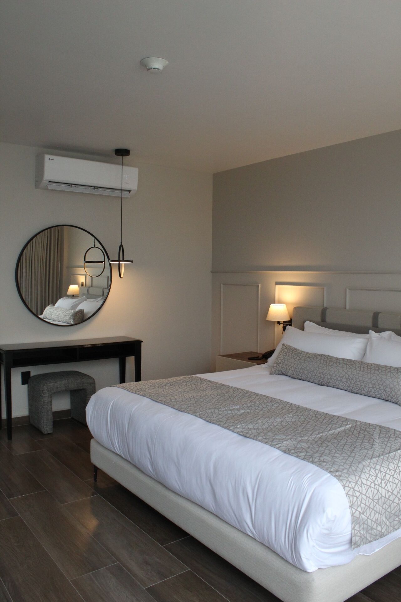 Ein Hotelzimmer mit einem großen Bett, einem runden Spiegel, einem Schreibtisch und einer Klimaanlage.