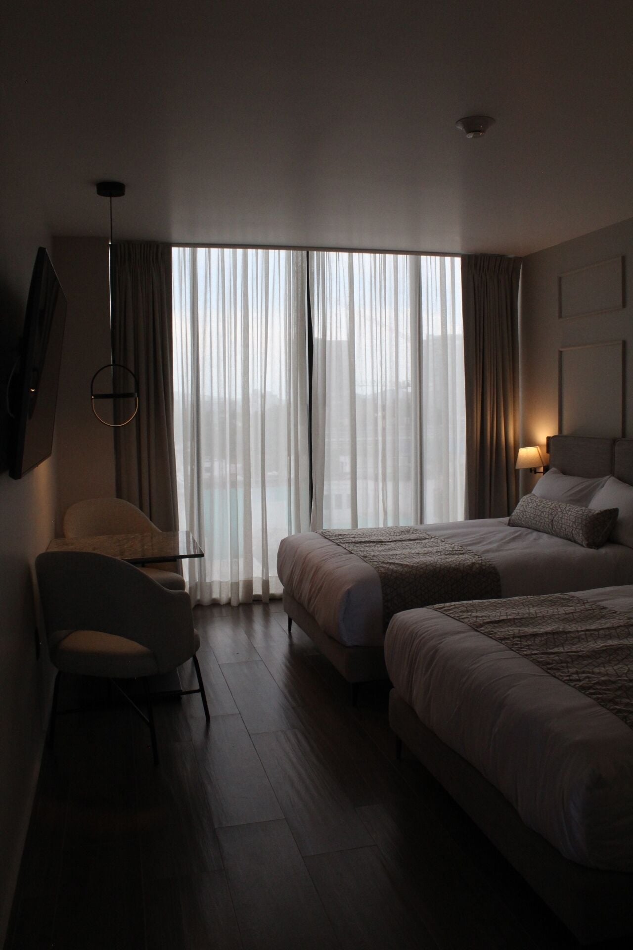 Ein Hotelzimmer mit großem Fenster, einem Bett, einem Sessel und einem Schreibtisch.