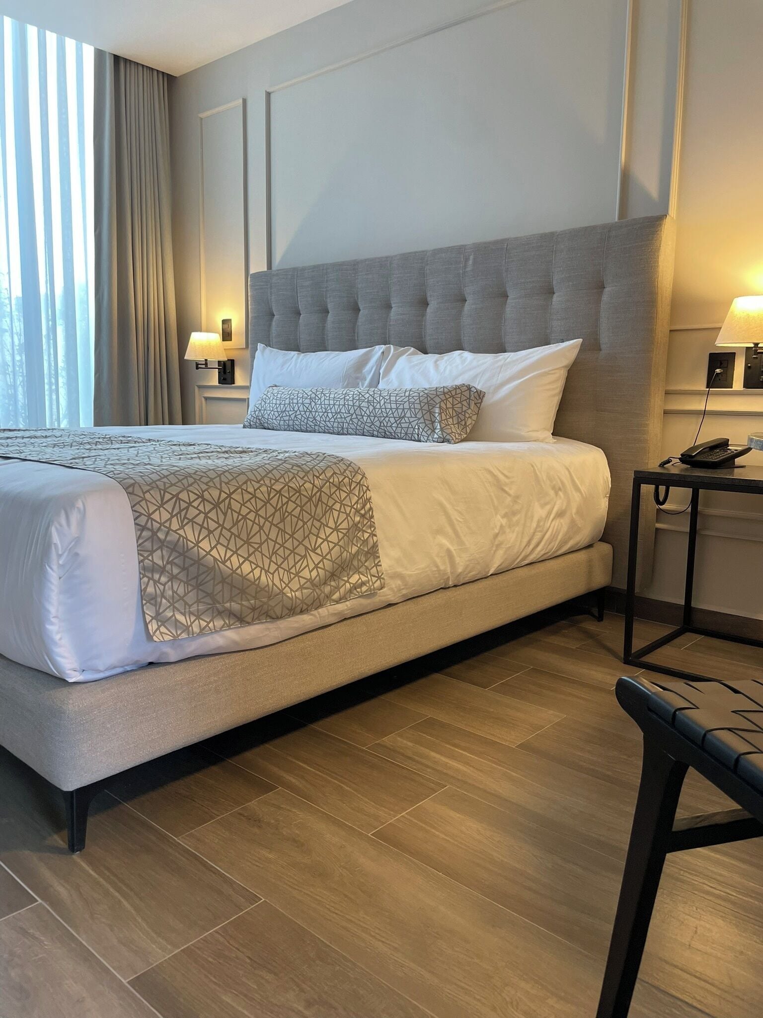 Una habitación de hotel con una cama grande, una mesita de noche con lámpara y una silla.