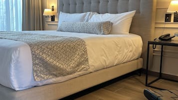 Una habitación de hotel con una cama grande, una mesita de noche con lámpara y una silla.
