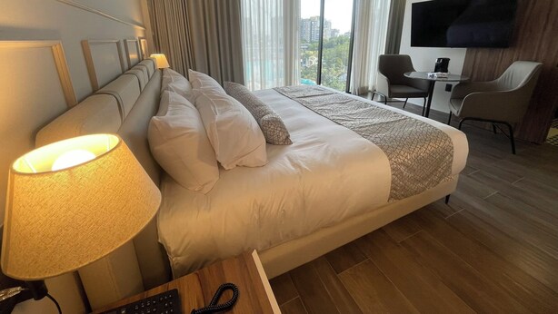 Habitación de hotel con una cama grande, un escritorio con una silla, televisión y vista a la ciudad.