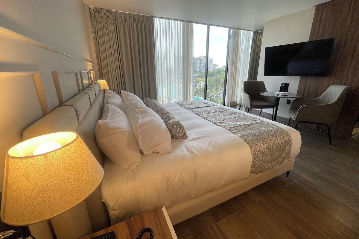 Een hotelkamer met een groot bed, een bureau met een stoel, een televisie en uitzicht op de stad.