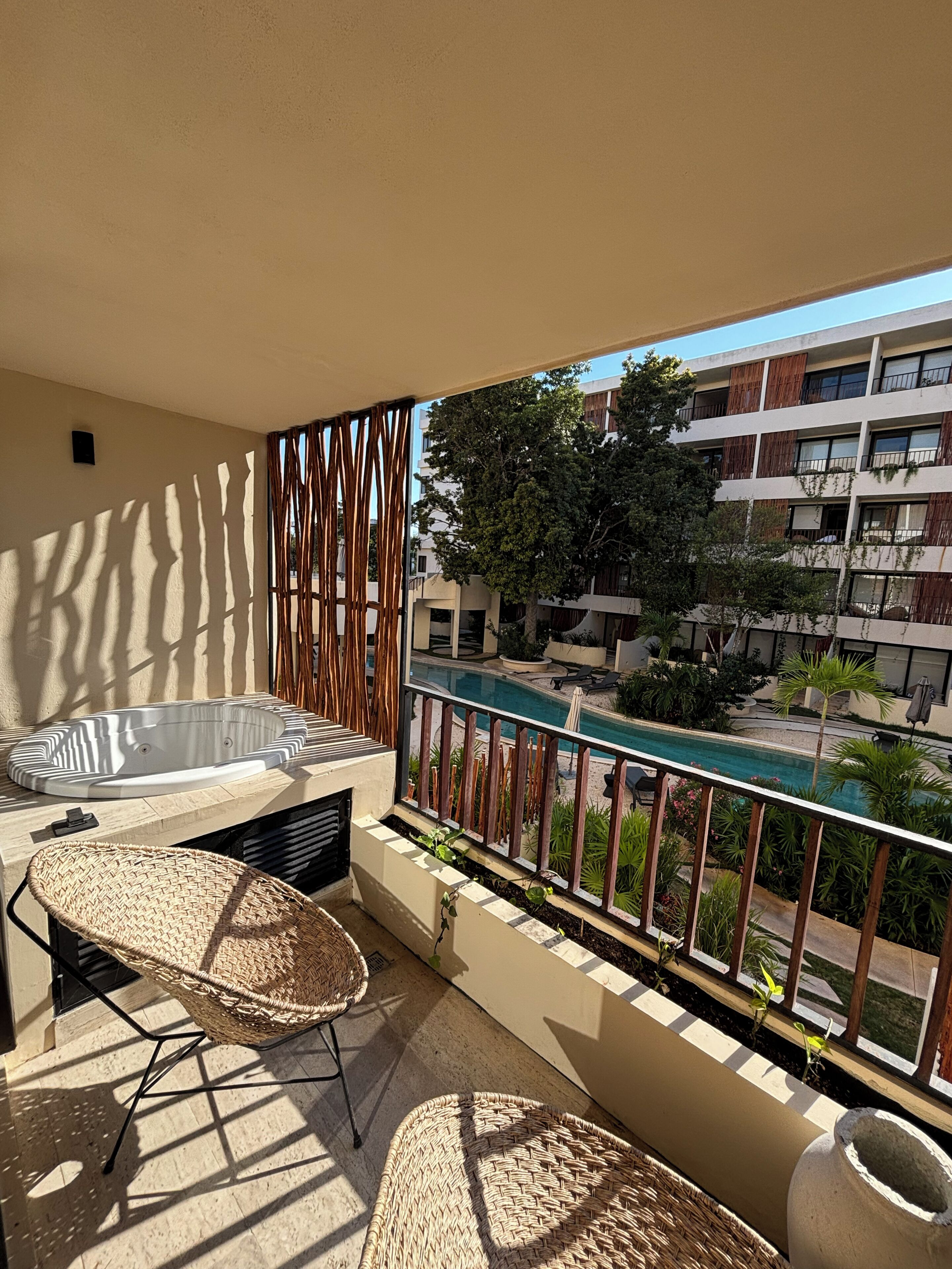 A balcony with a hot tub, wicker chairs, and a view of a swimming pool and buildings.
