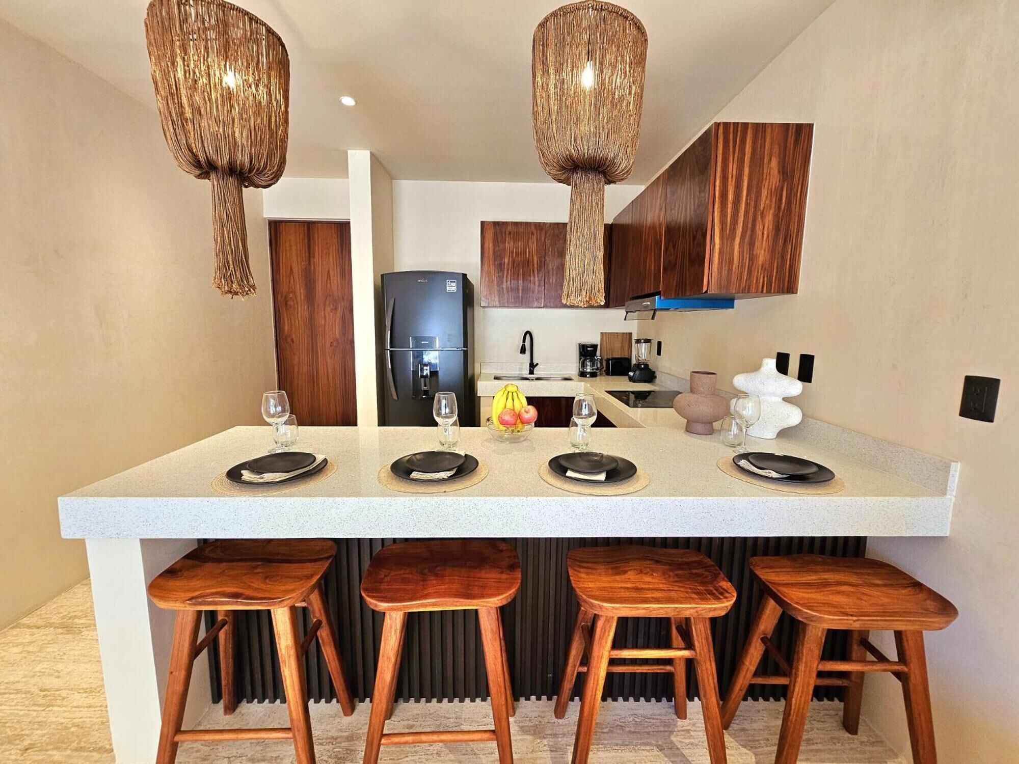 A modern kitchen with a central island, wooden stools, and pendant lights.