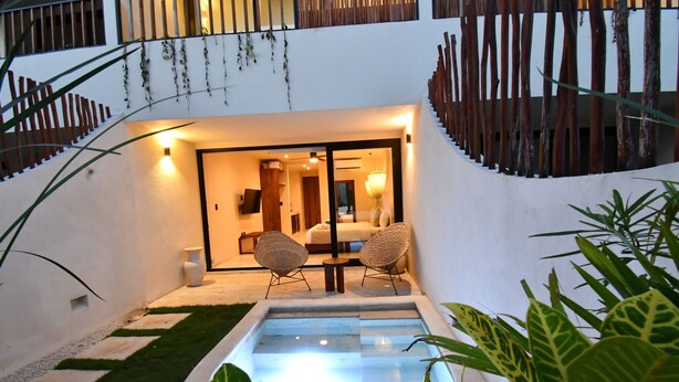A modern outdoor patio with a pool, two wicker chairs, and a well-lit interior visible through a glass door. - Loch Tulum by The Spot Rentals (Tulum)