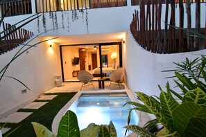 A modern outdoor patio with a pool, two wicker chairs, and a well-lit interior visible through a glass door. - Loch Tulum by The Spot Rentals (Tulum)