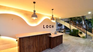 A reception desk with a wooden finish and a wave-like light design on the wall. - Loch Tulum by The Spot Rentals (Tulum)