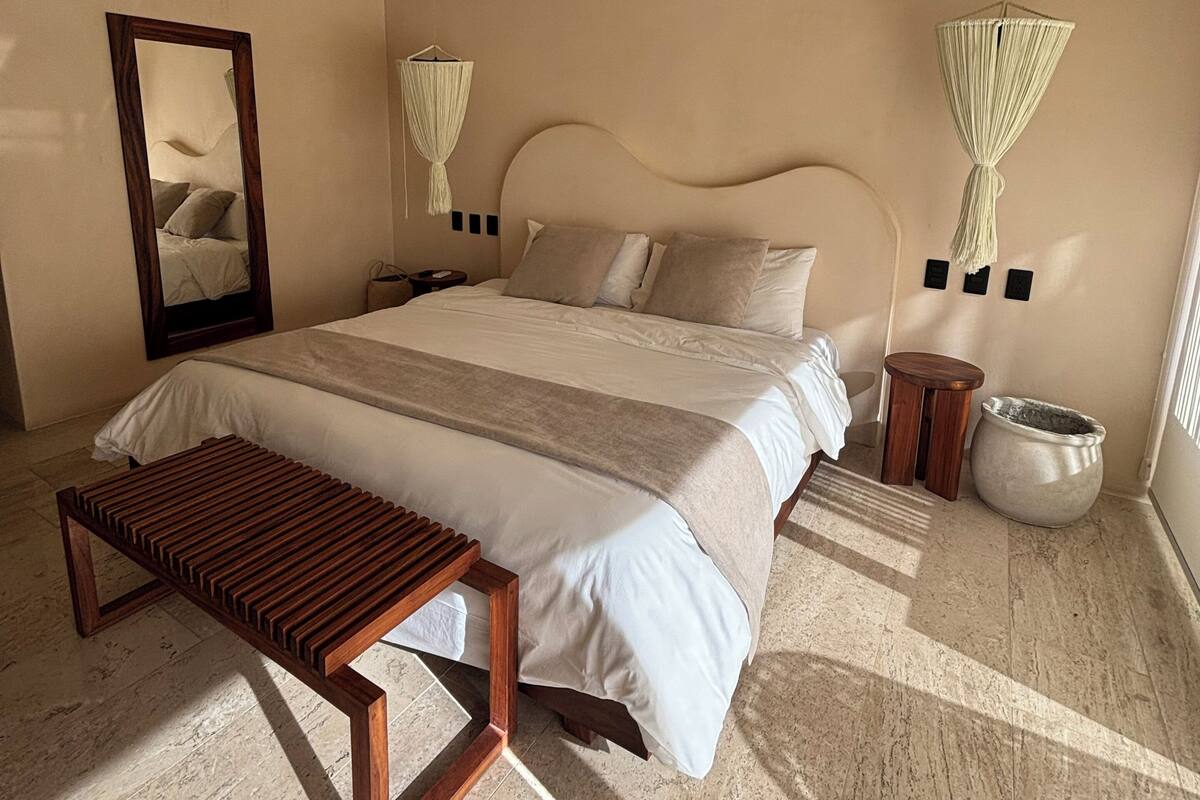 A bedroom with a bed, bedside tables, a ceiling fan, a mirror, and a hanging light fixture.