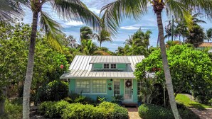 A small, single-story house with a green roof, surrounded by lush tropical vegetation. - Bahama Breeze Bungalow (West Palm Beach)