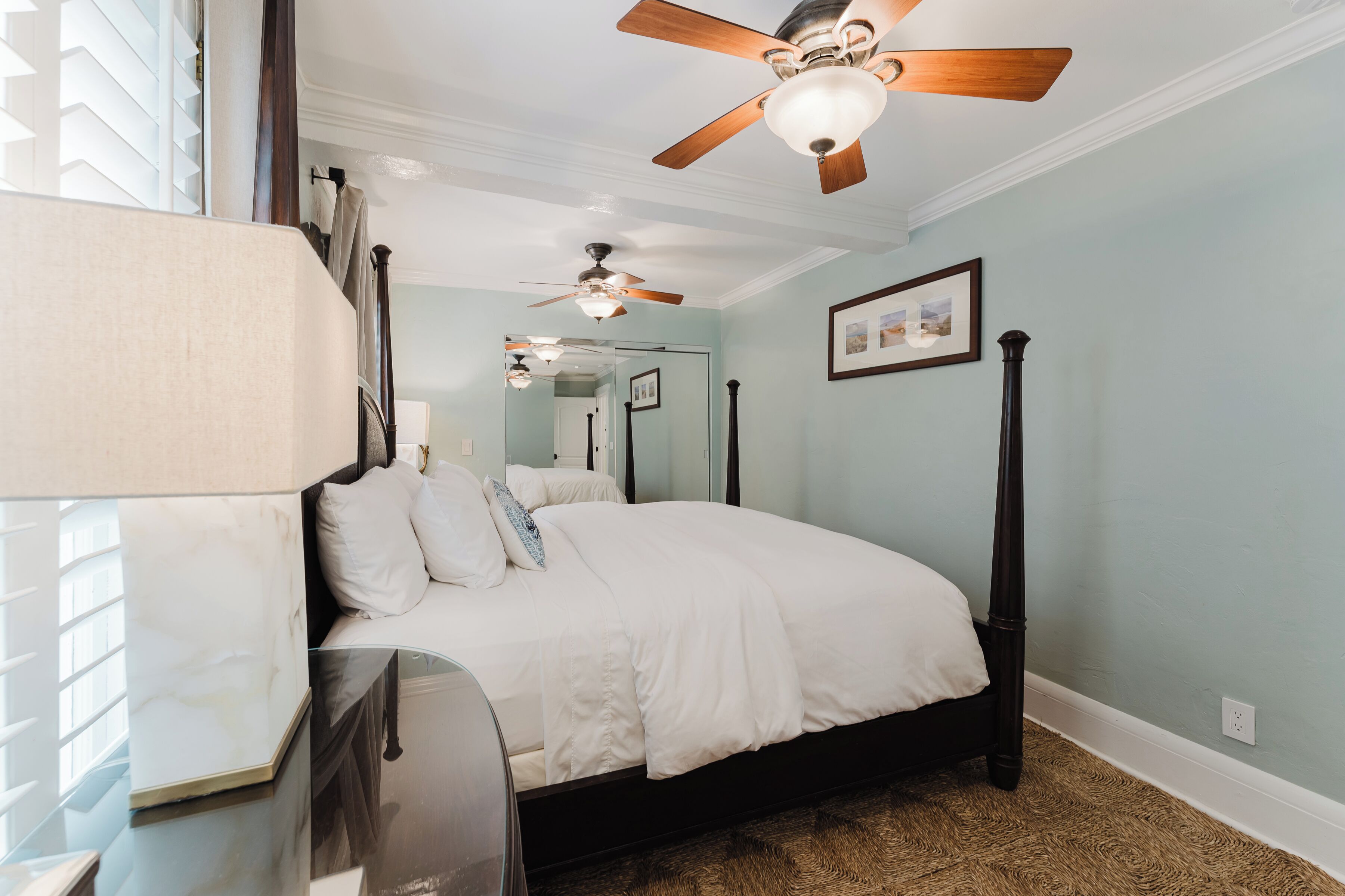 A bedroom with a bed, ceiling fans, a mirror, and a window with blinds.