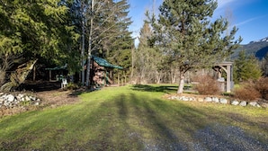 A rustic cabin with a green roof, surrounded by dense forest and a clear sky. - Making Lasting Memories While Enjoying This Unique Glamping Experience! (Deming)