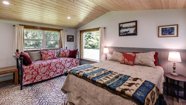 A bedroom with a wooden ceiling, a large bed with patterned bedding, a sofa with floral upholstery, and two windows with curtains. - Making Lasting Memories While Enjoying This Unique Glamping Experience! (Deming)