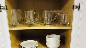 A cabinet with three shelves; the top shelf holds clear glass pitchers, the middle shelf has white plates, and the bottom shelf also has white plates.