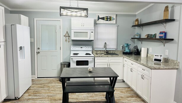 Une cuisine moderne avec des meubles blancs, un plan de travail noir, une cuisinière blanche et un luminaire suspendu.