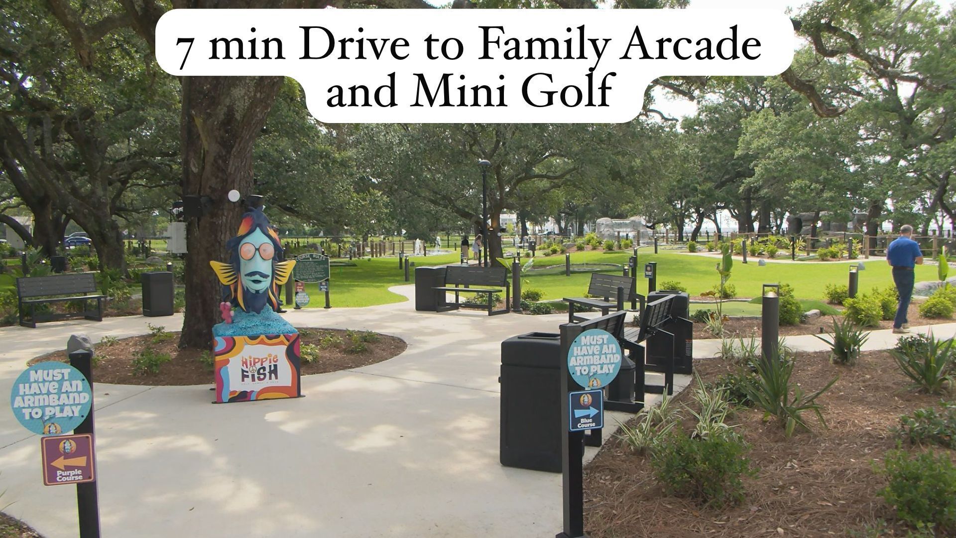 Un parco con una statua di pesce in stile hippie, tavoli da picnic e indicazioni che segnalano un viaggio in auto di 7 minuti per raggiungere Family Arcade e Mini Golf.
