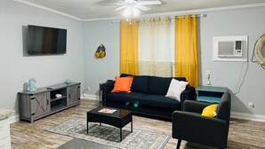 Un salon avec un canapé noir, une table basse, un téléviseur et un ventilateur de plafond.