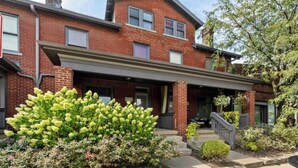 A two-story brick building with a covered front porch and a small garden area with yellow flowers. - Luxury Chefs Kitchen - OSU/Short North - Sleeps 10 (Columbus)
