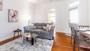 A modern living room with a grey sofa, a round coffee table, and a dining area with a wooden table and chairs.