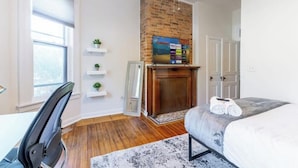 A bedroom with a brick fireplace, a bed, a desk, and a chair.