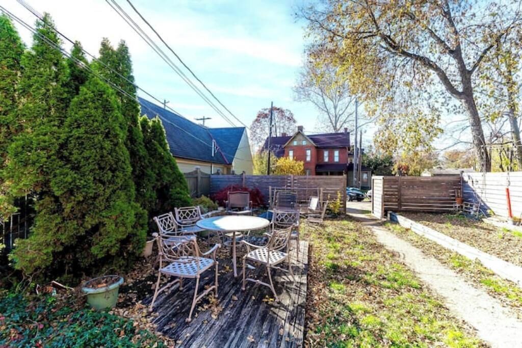 A backyard with a wooden deck, metal chairs, a small table, and a tall coniferous tree.