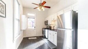 A kitchen with white cabinets, a stainless steel refrigerator, a microwave, and a ceiling fan.