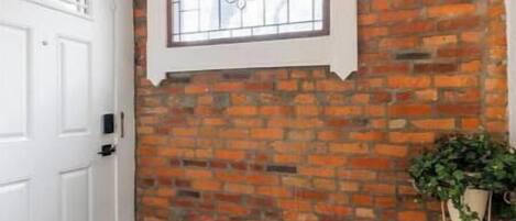 A room with a brick wall, a window with decorative glass, a white door, and a patterned rug.