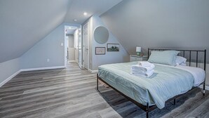 Ein Schlafzimmer mit schrägverdeckter Decke, einem Bett mit grüner Bettdecke, einem runden Spiegel und einem Nachttisch mit Lampe.