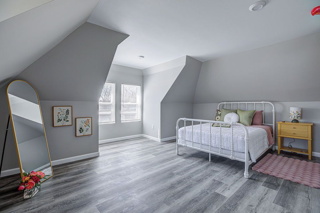 Une chambre avec un plafond en pente, un lit blanc, une table de chevet en bois et un miroir.